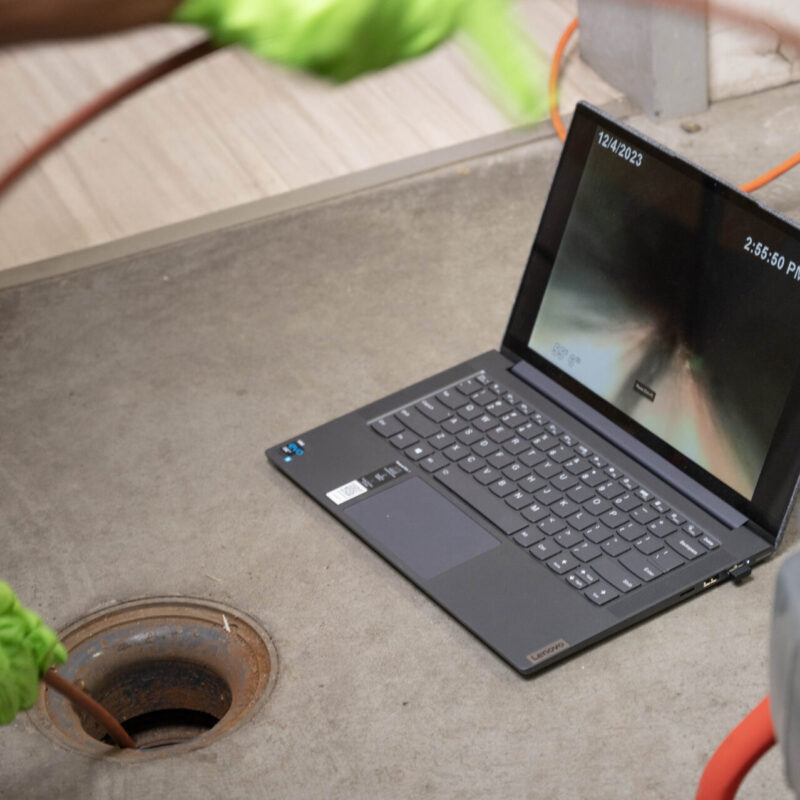 Professional sewer line inspection using a drain camera, displayed on a laptop screen, to detect blockages and damage in a residential plumbing system.